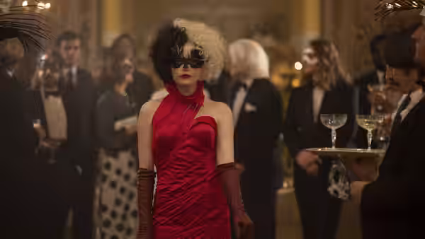 Cruella (Emma Stone) in a red gown and mask mingles with guests at a party