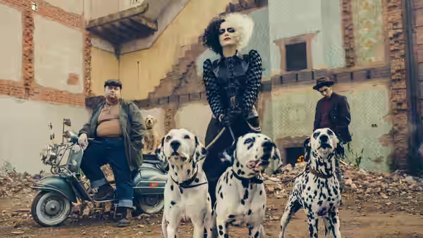 Cruella (Emma Stone) stands with three dalmatians in a debris-strewn courtyard