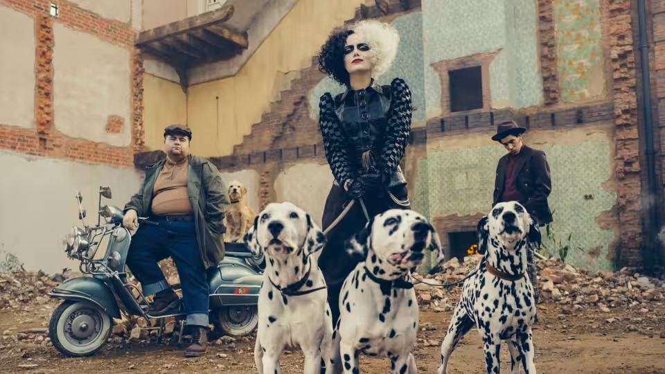 Cruella (Emma Stone) stands with three dalmatians in a debris-strewn courtyard