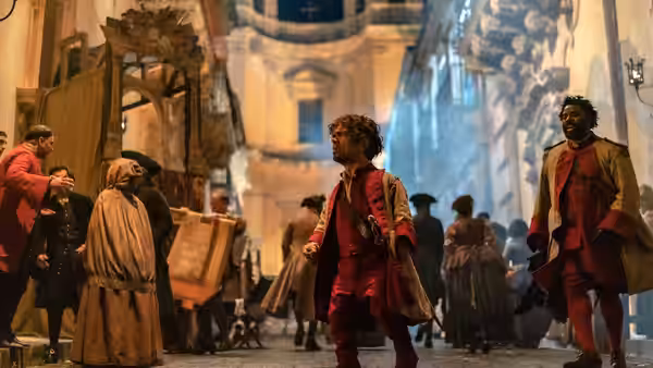 Cyrano (Peter Dinklage) walks through a crowded street as Christian (Kelvin Harrison Jr.) follows