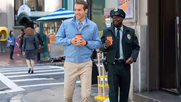 Guy (Ryan Reynolds) and Buddy (Lil Rel Howery) walk down a city sidewalk holding drinks