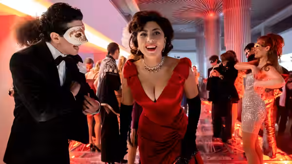 Patrizia Reggiani (Lady Gaga) leans toward a masked guest at a crowded party