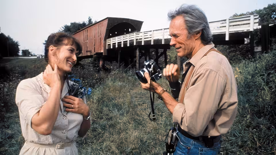 Francesca Johnson (Meryl Streep) smiles at Robert Kincaid (Clint Eastwood) by a covered bridge