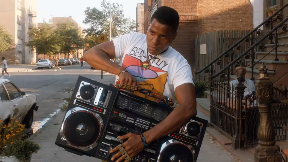 Radio Raheem (Bill Nunn) carries a large boombox on a city street