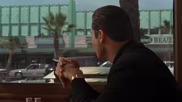 Chili Palmer (John Travolta) smokes a cigarette by a window overlooking the street