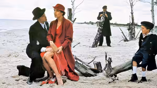 Agnes Matzerath (Angela Winkler) sits with a man on the beach as Oskar watches
