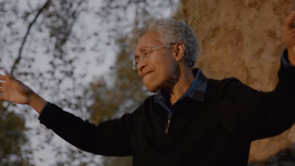 Beverly Glenn-Copeland (Beverly Glenn-Copeland) gestures with outstretched arms beside a tree