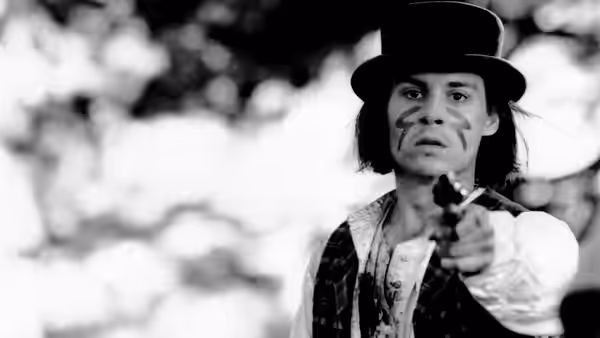 William Blake (Johnny Depp) points a pistol forward with face paint and top hat