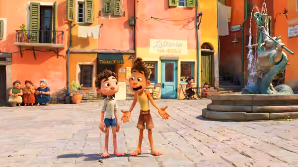 Luca and Alberto stand barefoot in a village square beside a fountain
