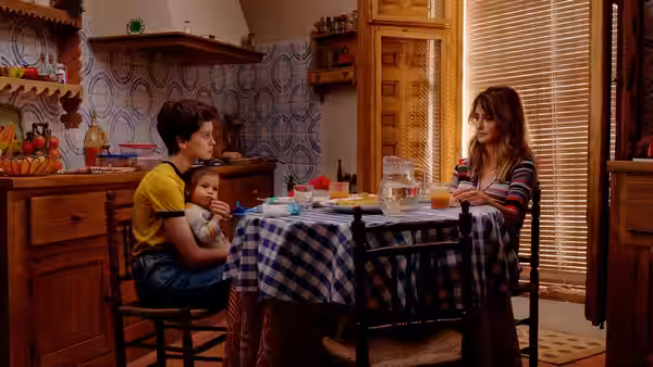 Ana (Milena Smit) holds a baby while Janis (Penélope Cruz) sits across the kitchen table