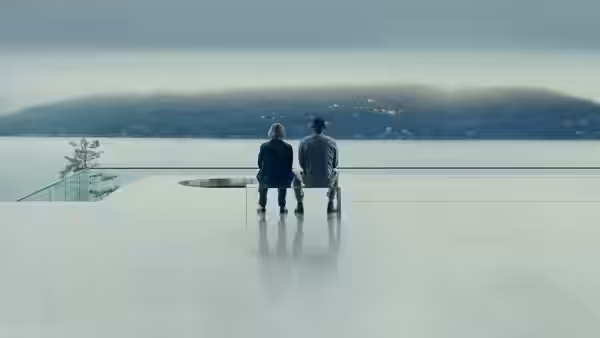 A woman and a man sit side by side, looking across a misty lake