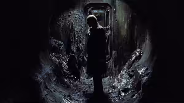A man stands in a dark flooded tunnel looking towards a doorway