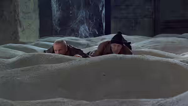 Two men lie hidden behind a dune in the ruined interior