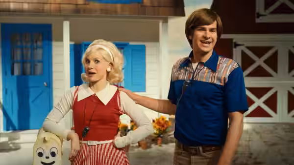 Tammy Faye Bakker (Jessica Chastain) and Jim Bakker (Andrew Garfield) stand outside a colorful house set