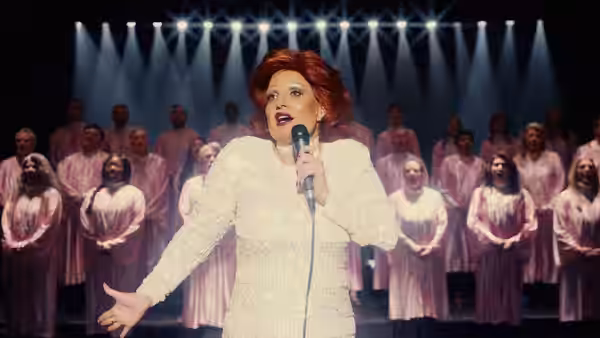 Tammy Faye Bakker (Jessica Chastain) sings into a microphone before a choir onstage