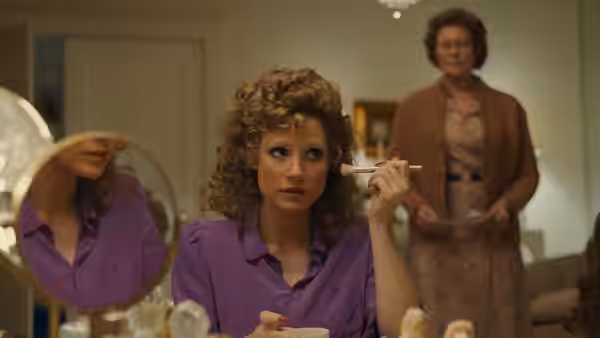 Tammy Faye Bakker (Jessica Chastain) applies makeup at a vanity as an older woman watches
