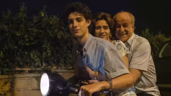 Fabietto Schisa rides a scooter between Maria and Saverio through a garden at night