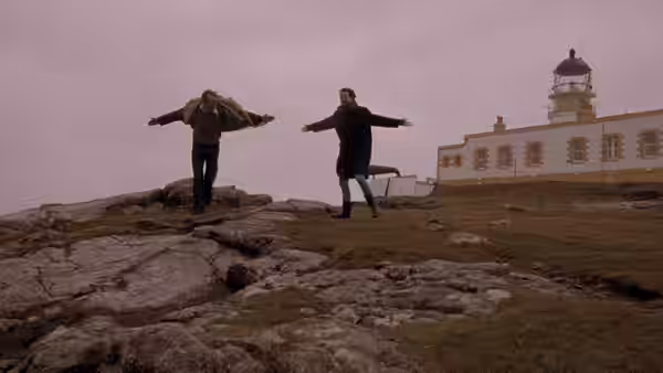 Jan (Stellan Skarsgård) and Bess (Emily Watson) with arms outstretched on a rocky hillside near a lighthouse