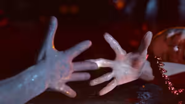 Two pale hands reach toward each other above a red-lit surface