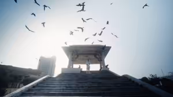 Two people stand beneath a rooftop pavilion as birds circle overhead