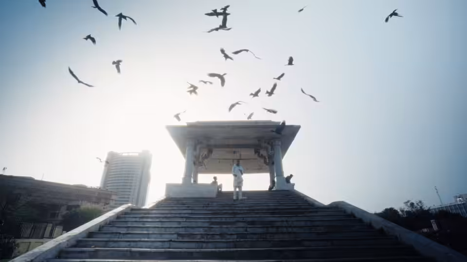 Two people stand beneath a rooftop pavilion as birds circle overhead
