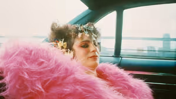 A person in a pink feathered coat reclines in a car