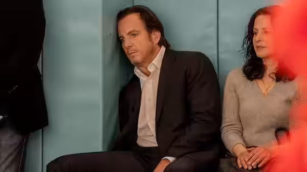 Alex Novak (Will Arnett) sitting against a blue wall beside a woman