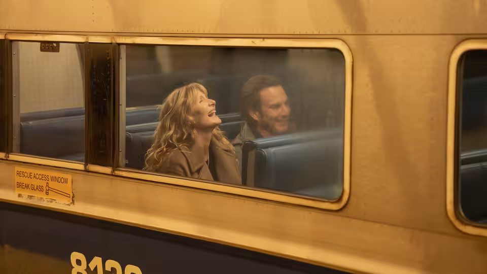 Tess Novak (Laura Dern) laughing beside Alex Novak (Will Arnett) on a train