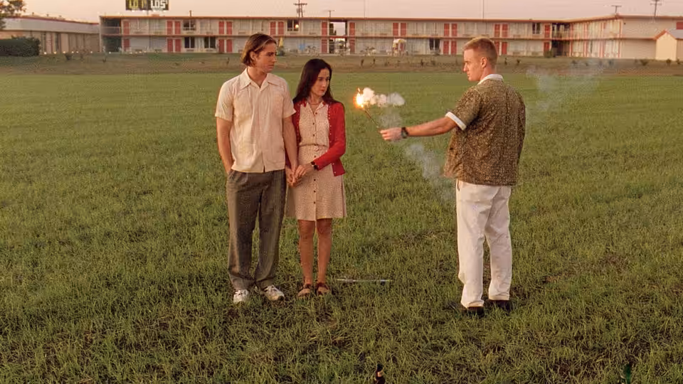 Anthony Adams (Luke Wilson) and Inez (Lumi Cavazos) watch Dignan (Owen Wilson) hold a lit sparkler in a field