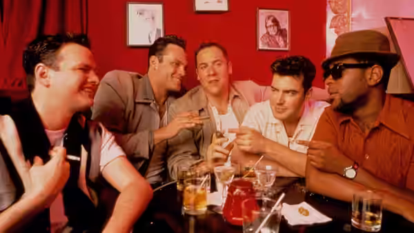 five men laughing and gesturing over drinks at a red booth table
