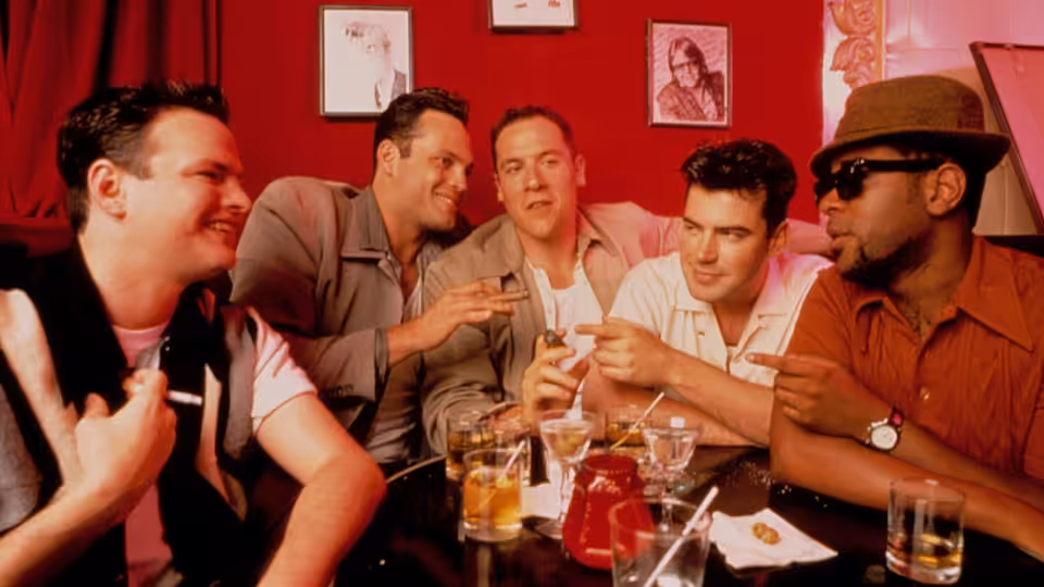 five men laughing and gesturing over drinks at a red booth table