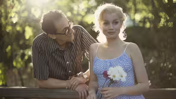 Marilyn Monroe (Ana de Armas) holds flowers beside a bespectacled man outdoors