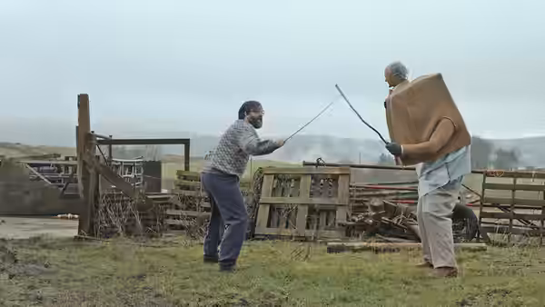 Brian (David Earl) and Charles (Chris Hayward) spar with sticks in a farmyard