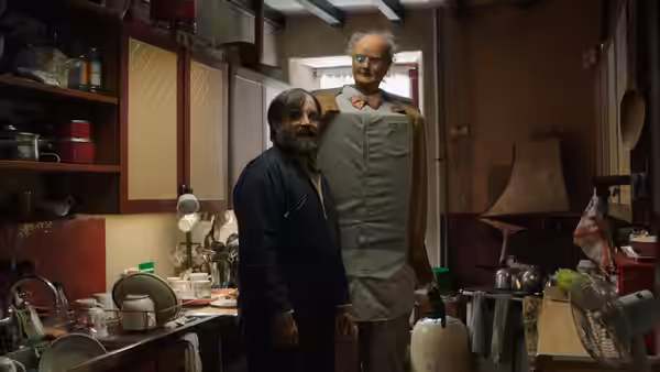 Brian (David Earl) stands beside Charles (Chris Hayward) in a cluttered kitchen