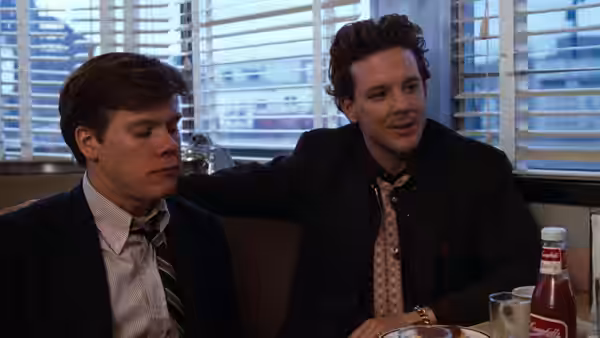 Two men at a diner table one with arm around the other