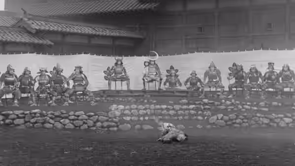 Armored samurai sit in a line atop a stone wall as a figure crawls below