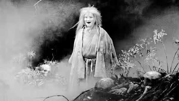 A pale forest spirit stands among plants and rocks, mouth open