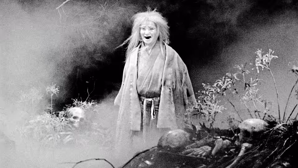 A pale forest spirit stands among plants and rocks, mouth open