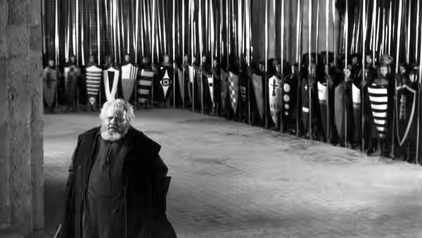 Falstaff (Orson Welles) stands before a wall of heraldic shields
