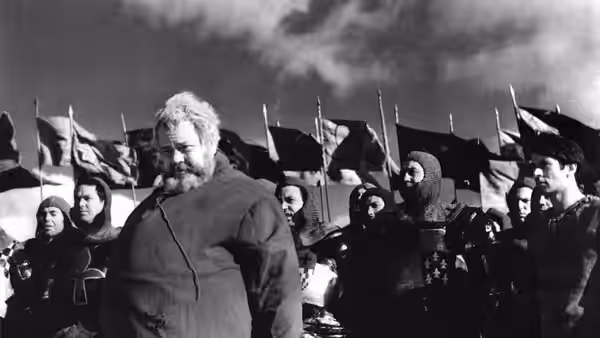 Falstaff (Orson Welles) walks before soldiers carrying banners