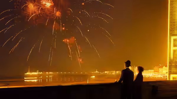 Two figures watch fireworks over the waterfront from a dark balcony