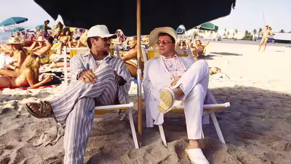 Agador (Hank Azaria) and Armand Goldman (Robin Williams) lounging on beach chairs under an umbrella