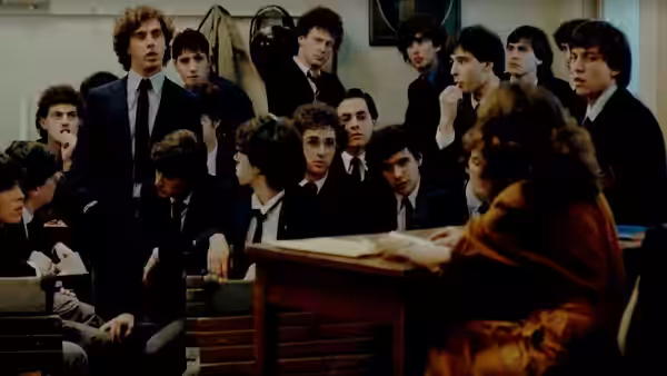 A woman addresses a crowded classroom of male students from behind a lectern