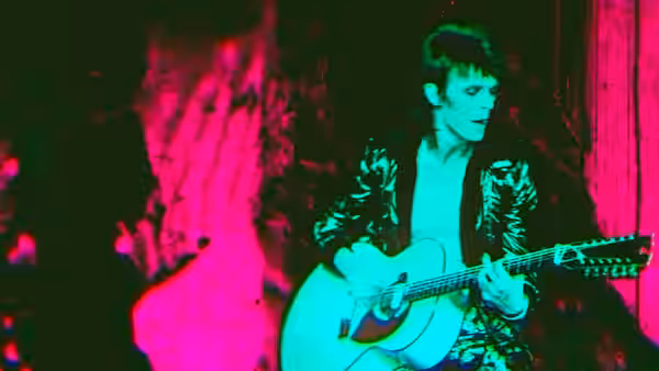 David Bowie (David Bowie) plays acoustic guitar under colored stage lights