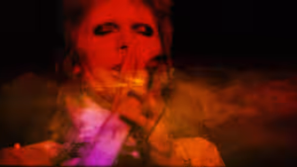 David Bowie (David Bowie) sings into a microphone in a red-lit close-up