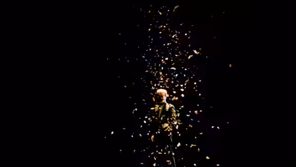 A lone performer stands beneath falling confetti in the darkness