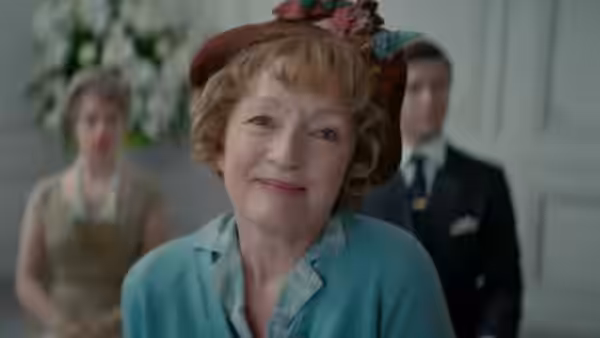 Ada Harris (Lesley Manville) smiles in a floral hat among fashion house staff