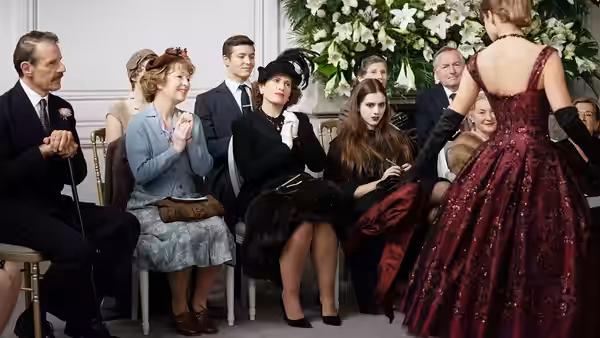 Ada Harris (Lesley Manville) applauds as a model presents a red gown to seated guests
