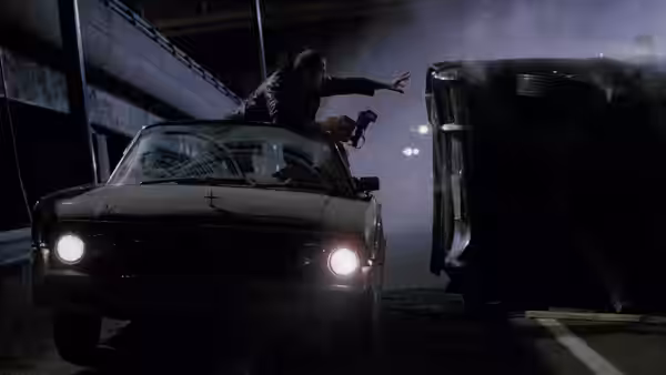 Vaughan (Elias Koteas) stands on car reaching toward overturned vehicle