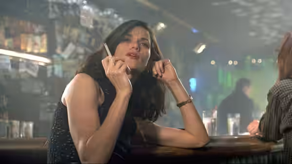 Bridget Gregory (Linda Fiorentino) leans at a bar, holding a cigarette beside a crowded lounge